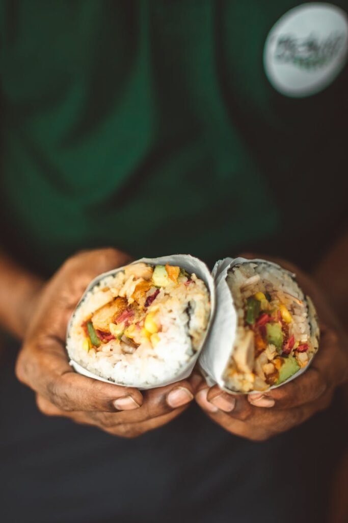 Close-up of hands holding a freshly made burrito filled with rice and vegetables.