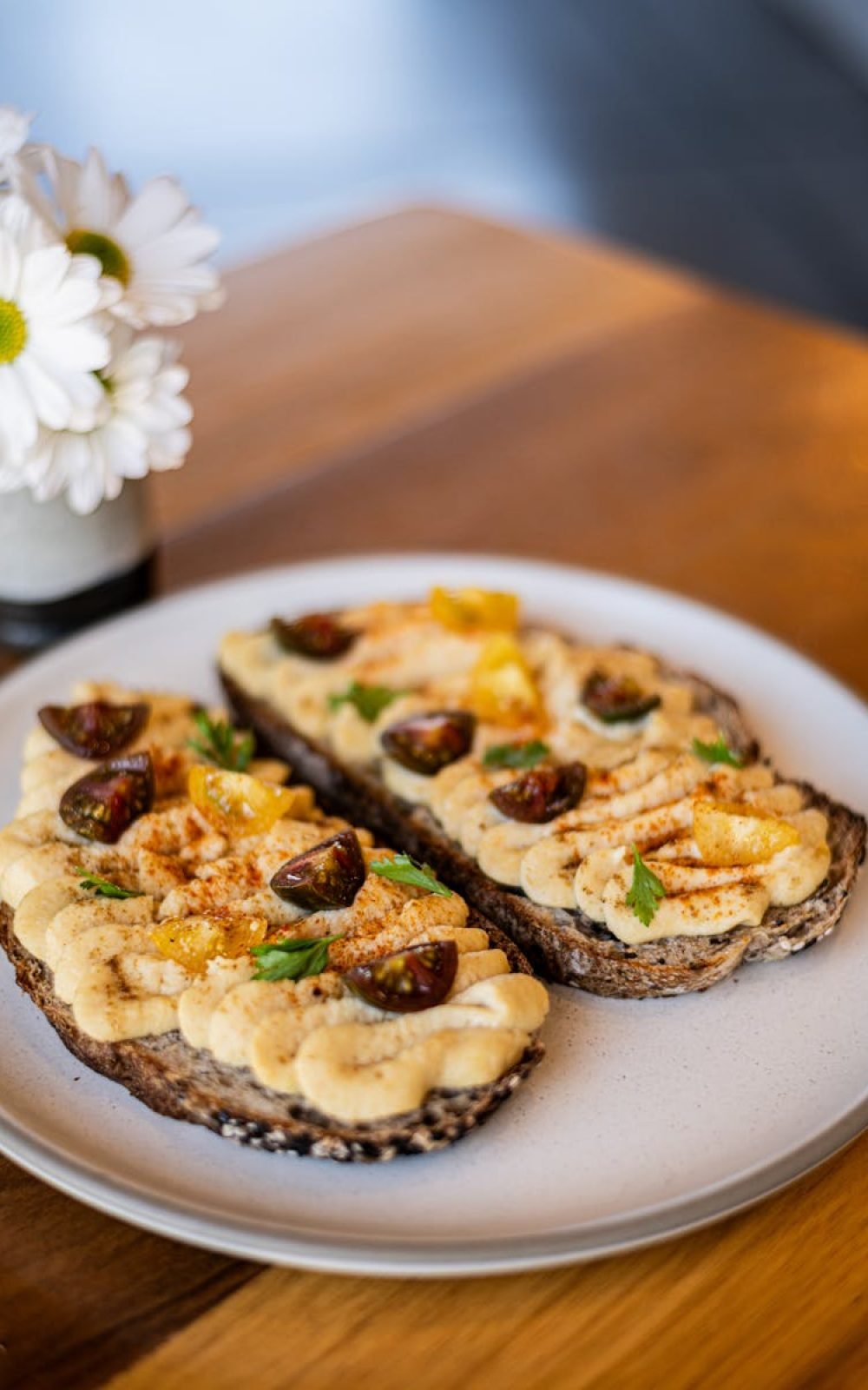 Delicious gourmet hummus crostini with cherry tomatoes and herbs, styled neatly on a plate.